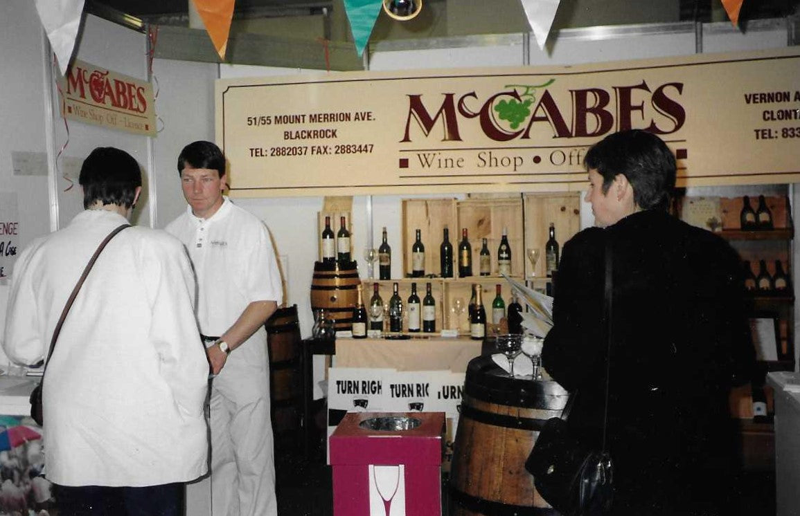 People interacting with a McCabes Wine Shop display featuring wine bottles and barrels.
